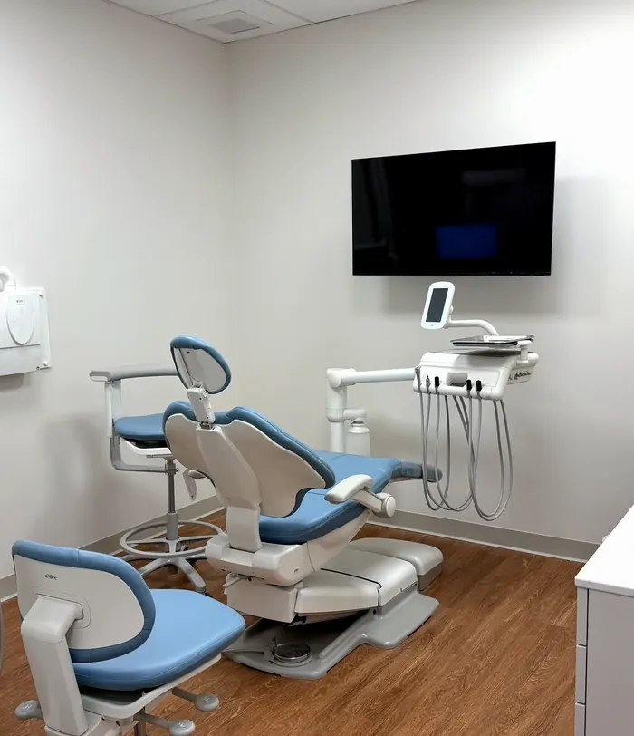 A bright treatment room with blue dental chairs and a wall-mounted television.