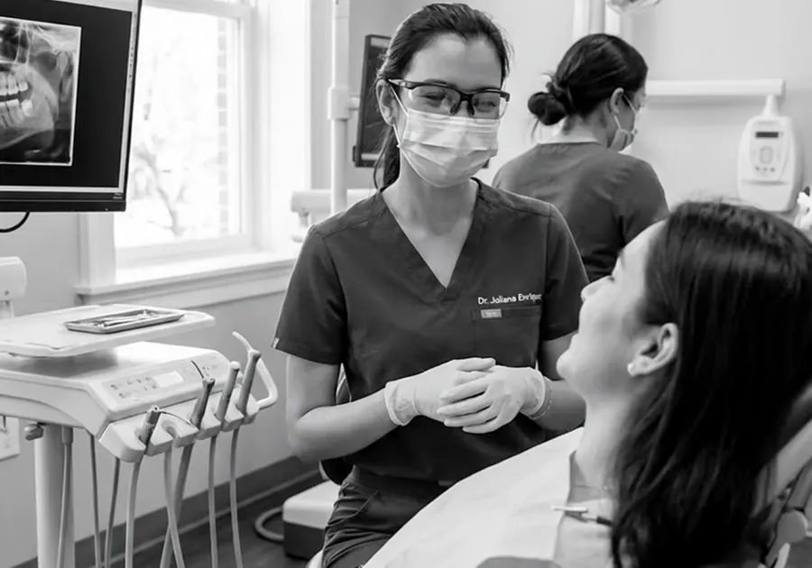 Dr. Juliana Enriquez talking with a patient in the chair, with dental images on the monitor beside them.